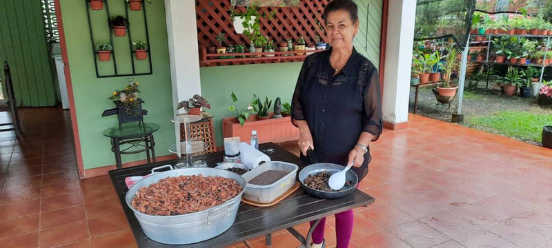 A woman poses in front of a table filled with various cacao and chocolate dishes, highlighting a rich culinary experience.