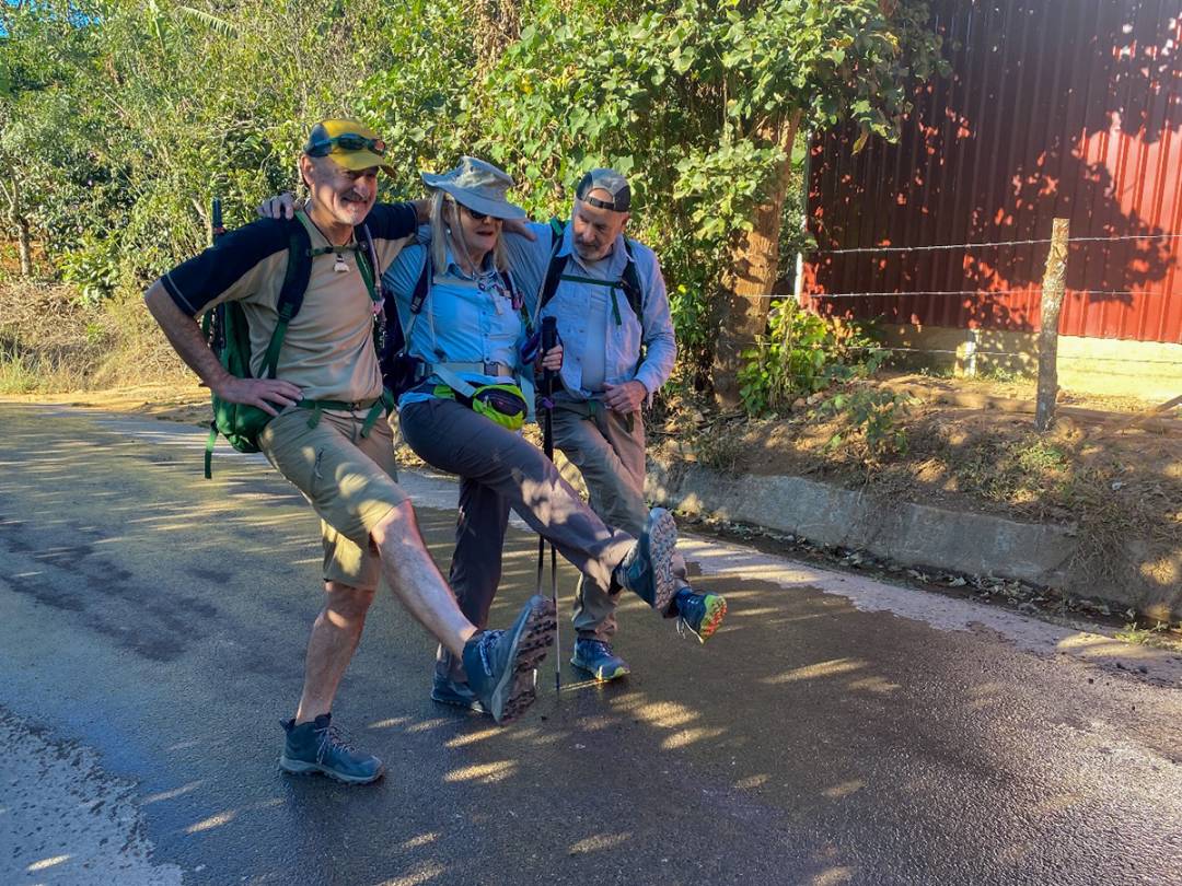 Three hikers with backpacks walking along a scenic road, surrounded by nature and ready for an adventure.