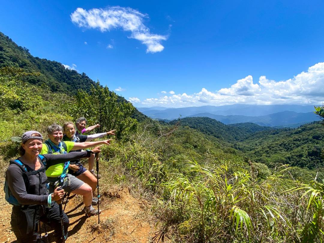 Four enthusiastic hikers on a mountain trail, arms outstretched, enjoying the breathtaking views and fresh air.