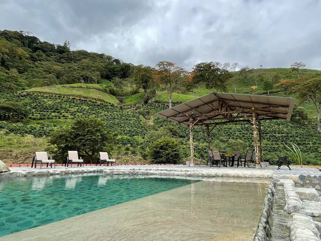 A serene pool surrounded by chairs and a gazebo, nestled against a picturesque hillside backdrop.