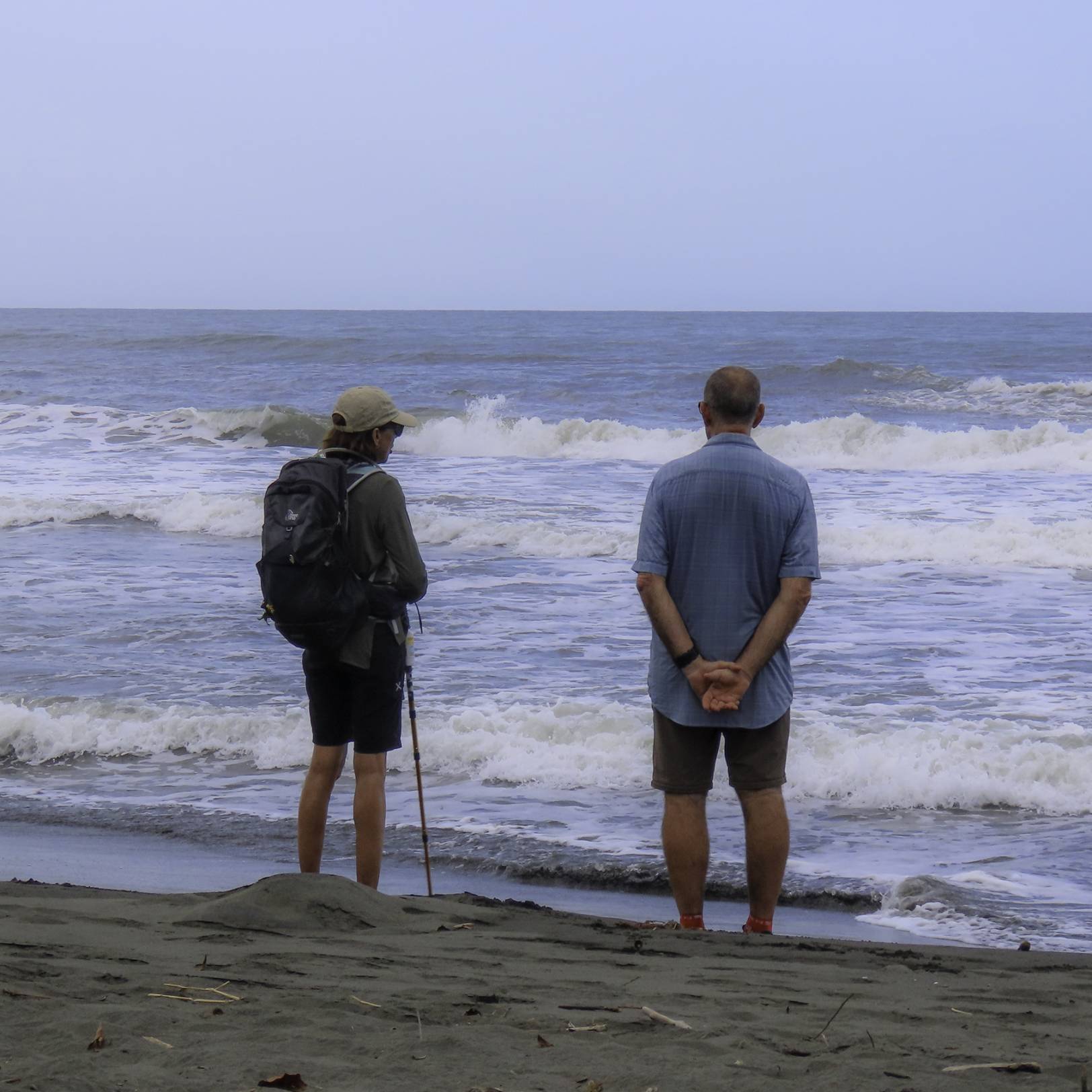 Two hikers standing on a sandy beach, enjoying the scenic view of the ocean and the clear blue sky.