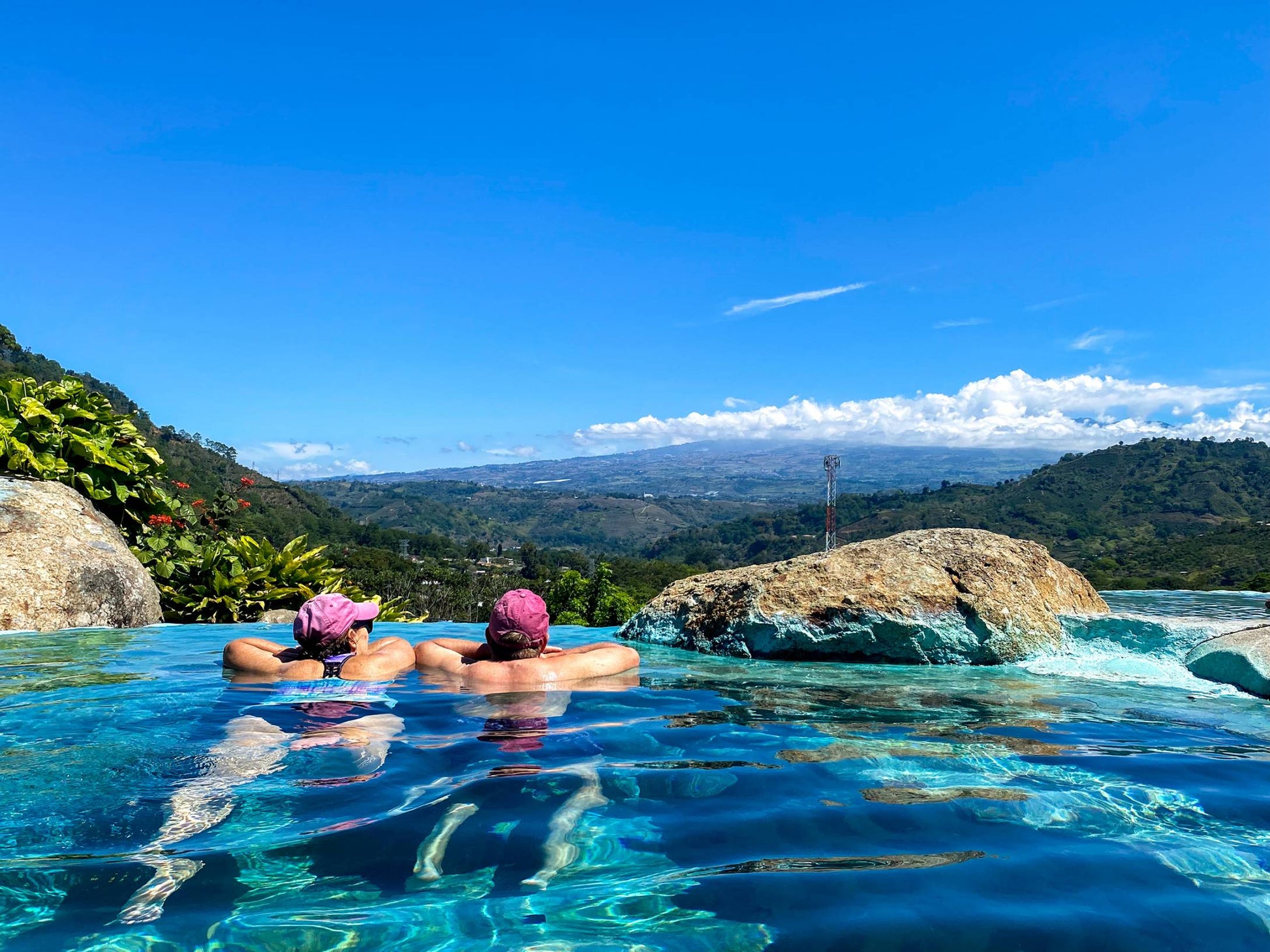 Two individuals enjoying a refreshing swim in a pool, surrounded by a stunning mountain landscape in the background.